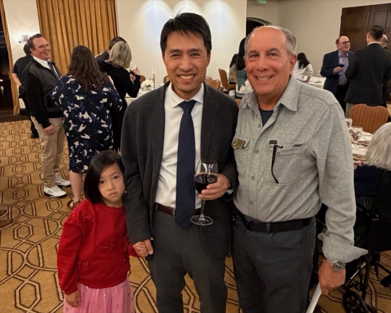 Bob Nguyen in a suit at the Millbrae Person of the Year award ceremony, standing with a guest and his daughter