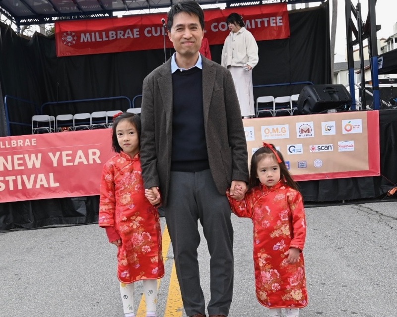 Bob Nguyen holding hands with his two daughters, dressed in red qipao, in front of the Millbrae Lunar New Year Festival stage