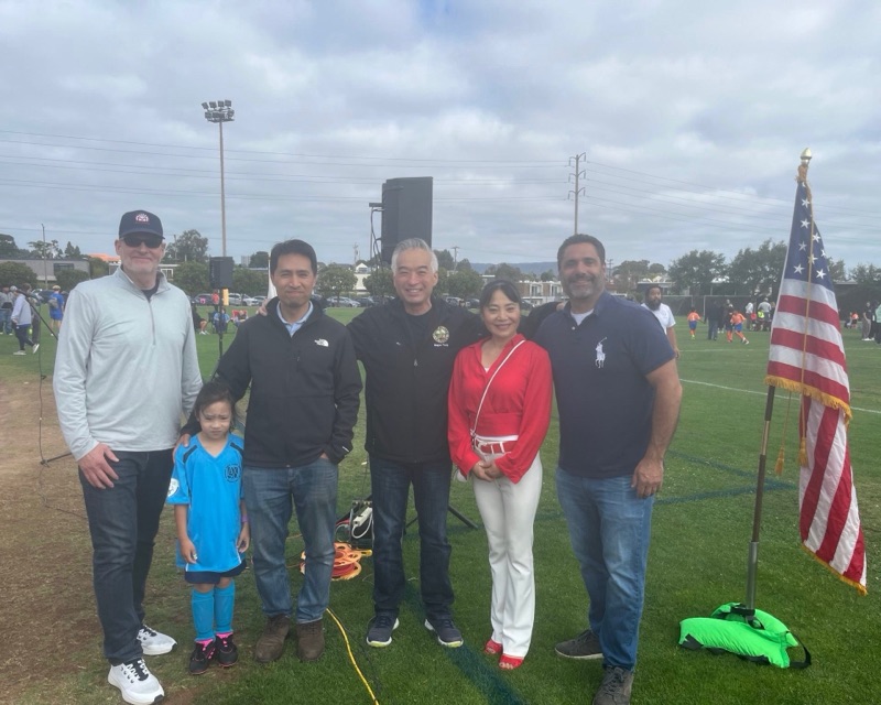 Bob Nguyen with neighbors and a young player beside the American flag at AYSO youth soccer opening day